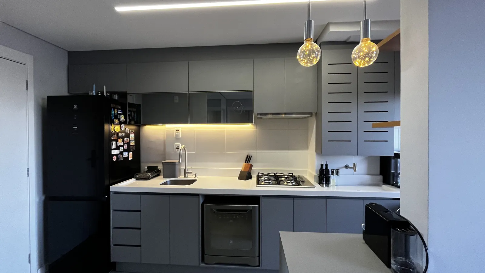 Cozinha planejada cinza com bancada clara, iluminação embutida e pendentes