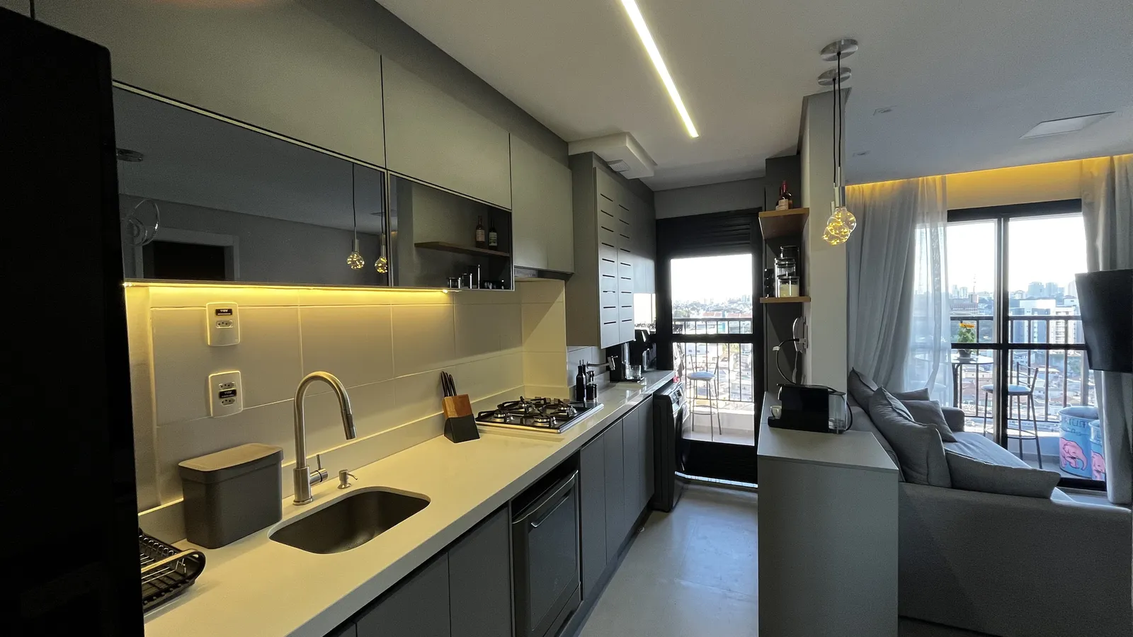 Cozinha planejada em grafite com iluminação sob os armários, integrada à sala